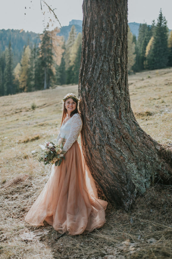 Bride is leaning on a tree in a forest in Northern Italy