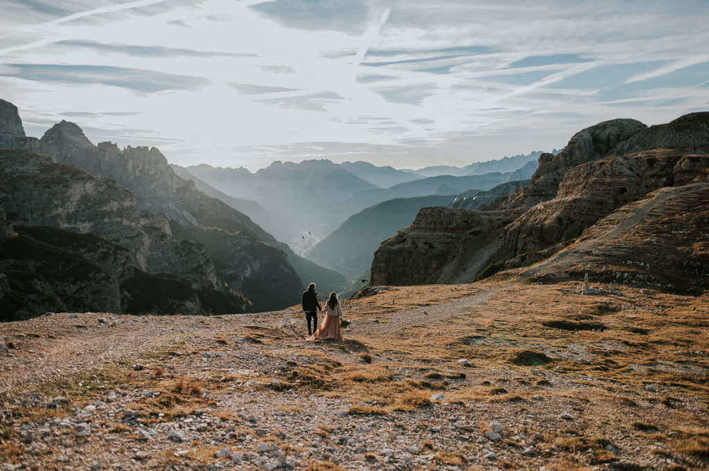 Bride and groom walking among stunning mountain landscapes in Italian Dolomites on a warm and sunny october day captured by Dolomites wedding photographer 