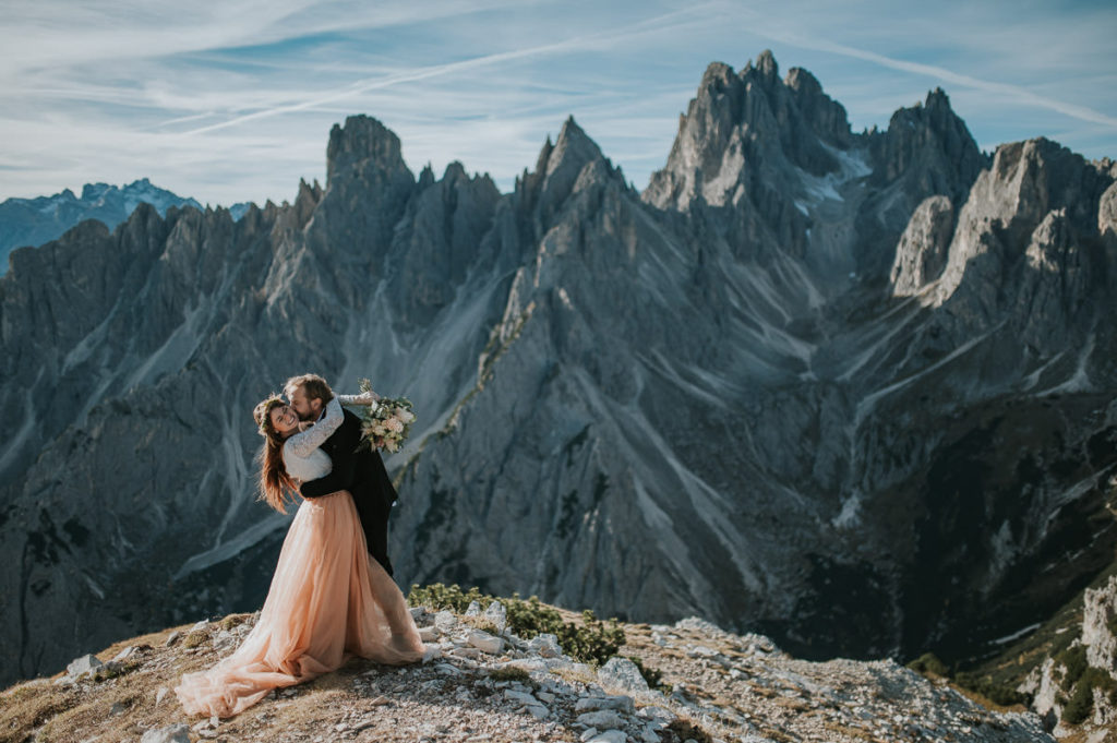 Wedding anniversary in Italian Dolomites in Northern Italy - the groom is kissing her on her chick and she is laughing 