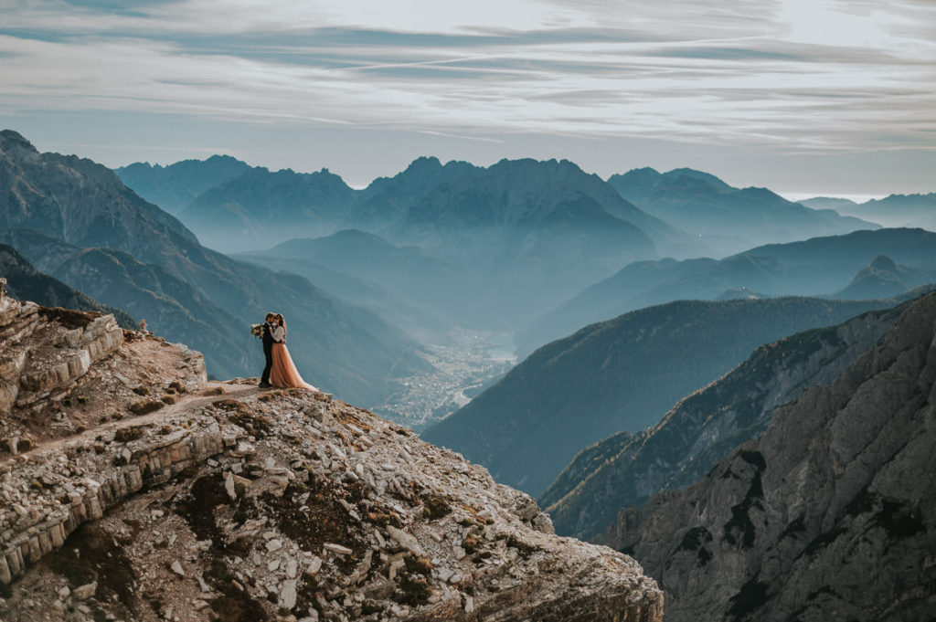 Bride and groom standing on a cliff in mountains of Northern Italy - captured by Dolomites wedding photographer TS Foto Design 