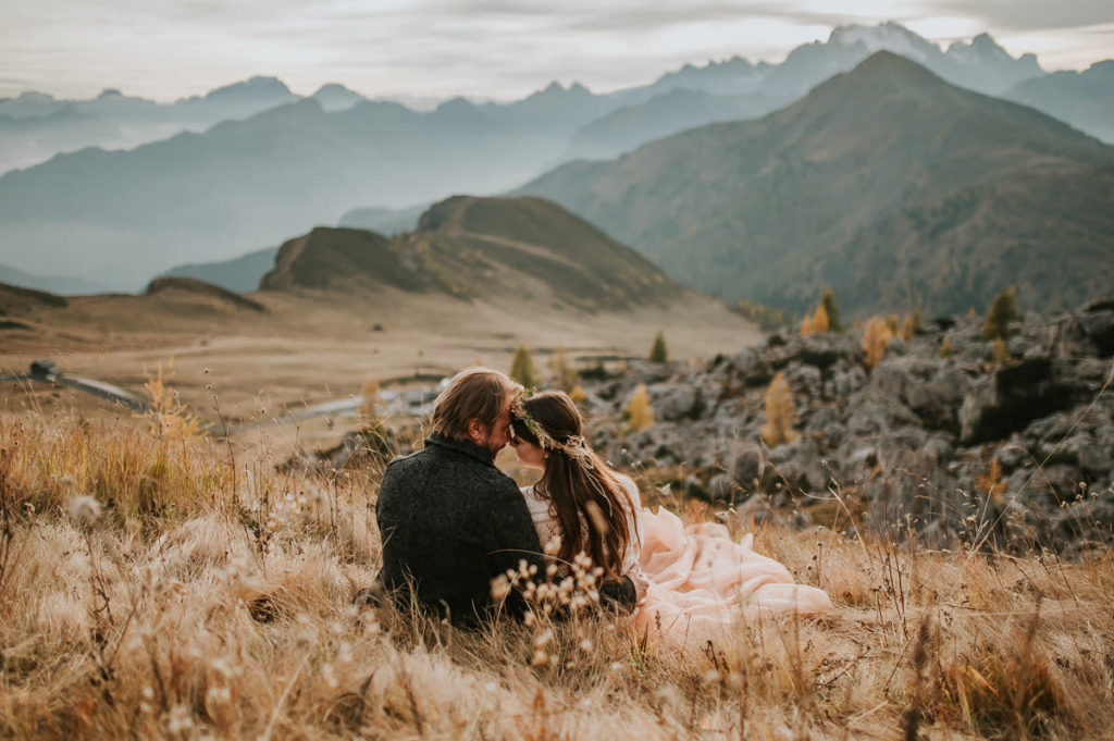 Bride and groom sitting in a dry grass field with a stunning mountain view in Northern Italy - by dolomites elopement wedding photographer TS Foto Design