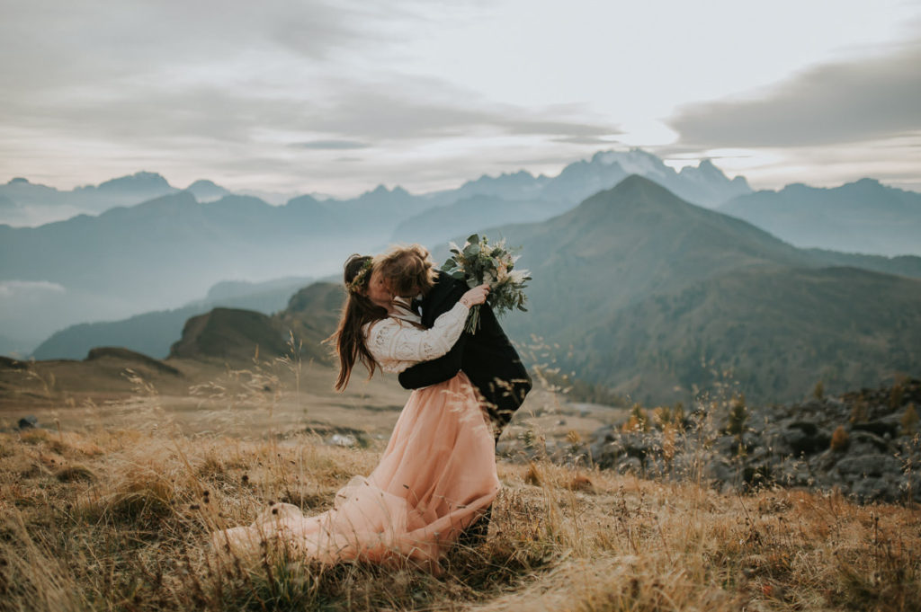 Bride and groom kissing in a field with a stunning mountain view in Northern Italy - by dolomites elopement wedding photographer TS Foto Design