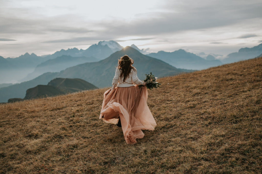 Beautiful bride running into the sunset with a stunning mountain view of Italian Alps - captured by Dolomites wedding photographer