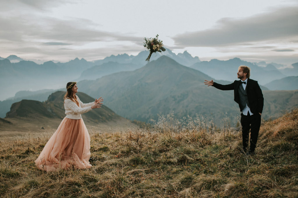 Groom throwing a bridal bouquet to his bride among stunning views of Italian Dolomites