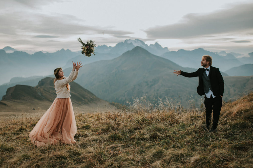 Groom throwing a bridal bouquet to his bride among stunning views of Italian Dolomites - by dolomites wedding photographer TS Foto Design