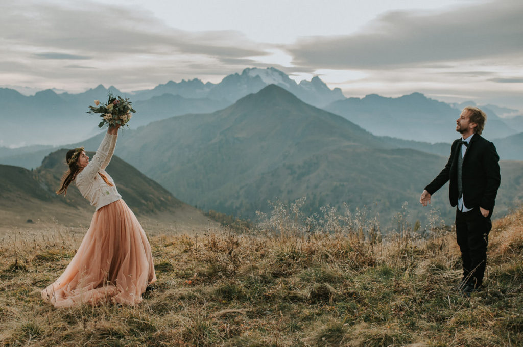 Groom throwing a bridal bouquet to his bride among stunning views of Italian Dolomites