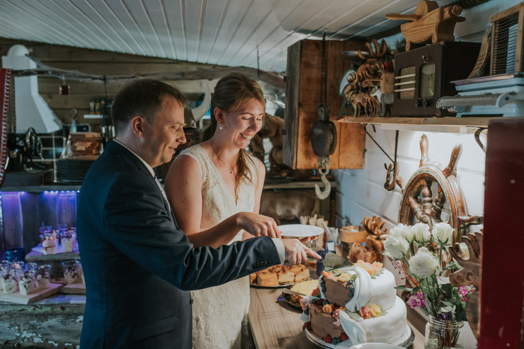 Bride and groom cutting a cake together on their wedding day in  a rustic styled wedding reception location in Storekorsnes Alta Norway