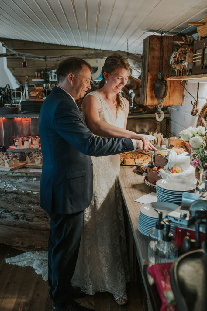 Bride and groom cutting a cake together on their wedding day in  a rustic styled wedding reception location in Storekorsnes Alta Norway