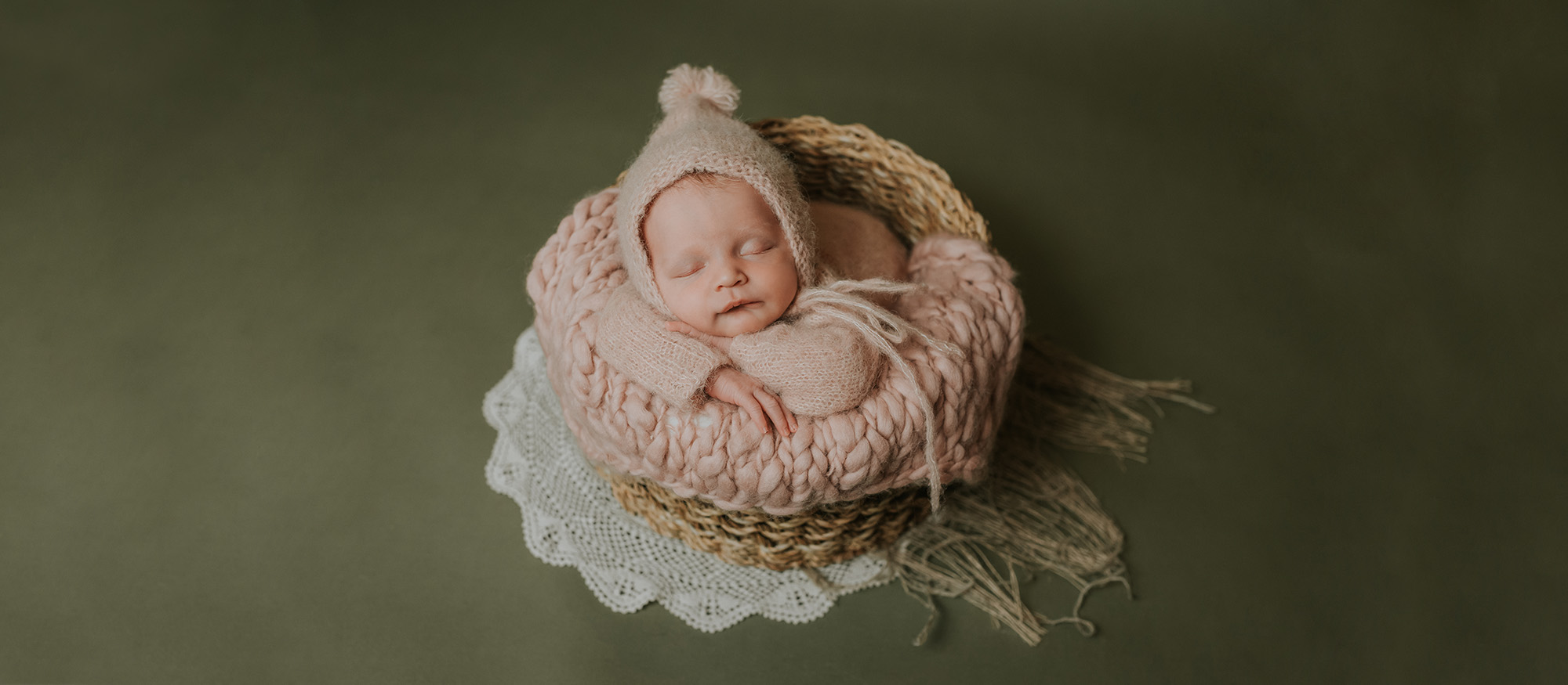 Søt nyfødt jente med rosa strikket klær sover i en kurv på grønn bakgrunn