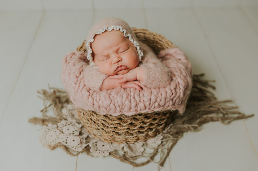Nyfødt jente i en rosa ull drakt sover fredelig på nyfødtfotografering