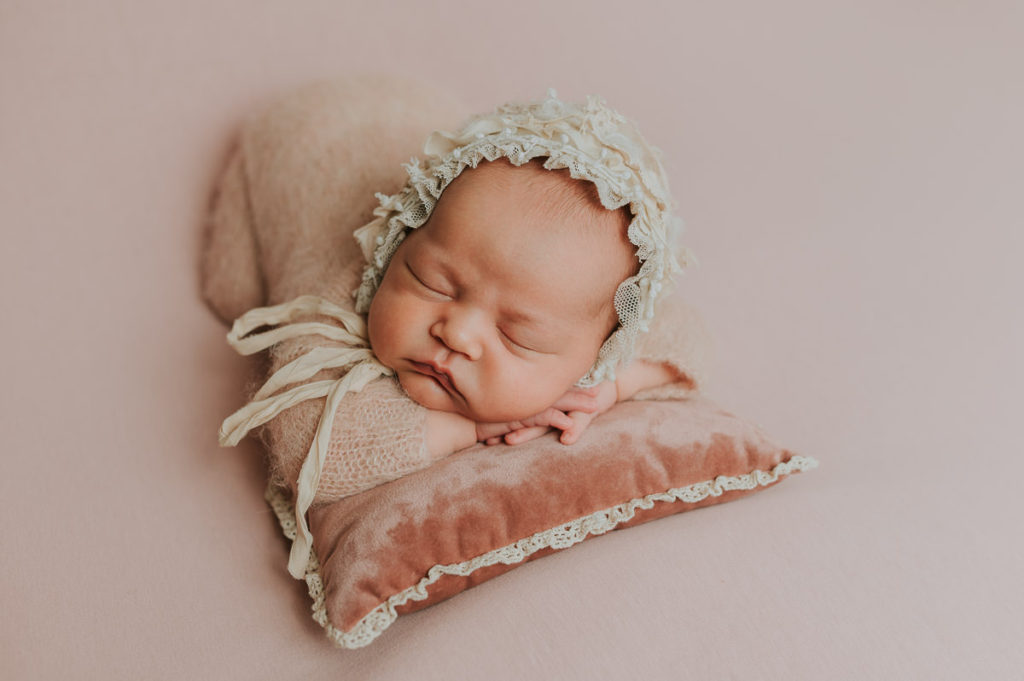 Nyfødt jente i en rosa ull drakt sover fredelig på nyfødtfoto i Alta