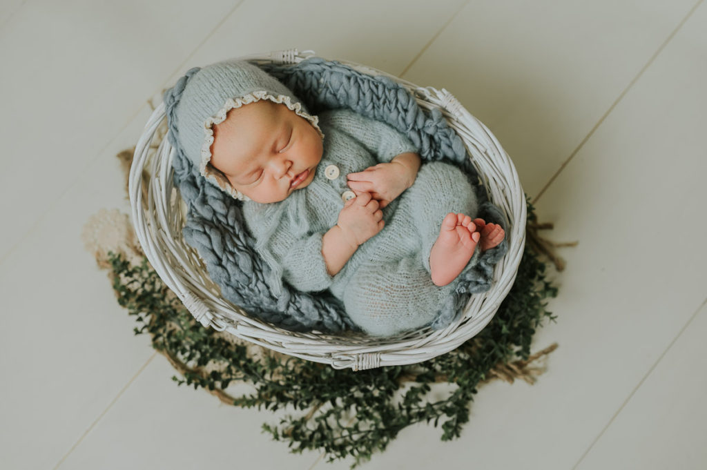Nyfødt jente i lyseblå strikket drakt sover på nyfødtfotografering i fotostudio i Alta