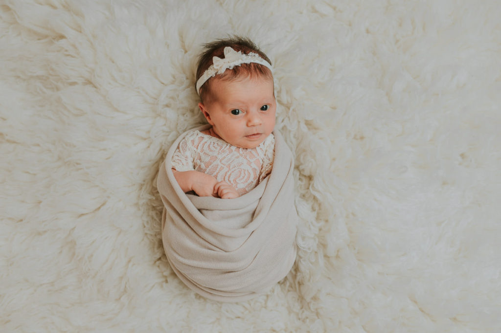 Nyfødtfotografering i beige farge nyanser hvor babyen er lysvåken og ser rett inn i kamera