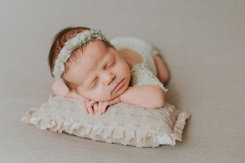 Nyfødt jente sover søtt på en beige fotobakgrunn