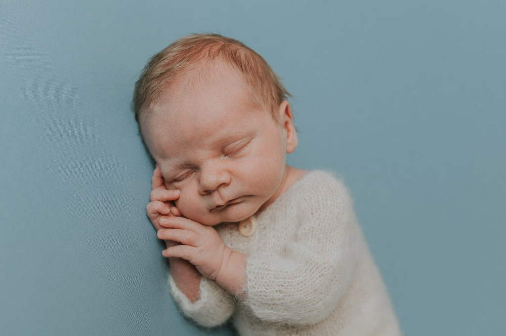 Nyfødt gutt i en hvit ulldrakt sover på en lyseblå fotobakgrunn i fotostudio i Alta på nyfødtfoto