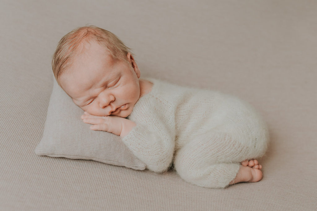 Søt liten nyfødt gutt sover på en pute på beige bakgrunn - nyfødtfotografering i Alta