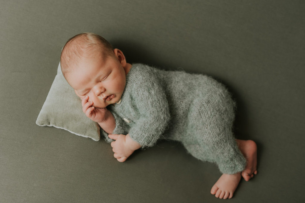 Nyfødt gutt i grønn strikket drakt  sover på grønn bakgrunn og en liten pute på nyfødtfotografering i Alta hos TS Foto Design