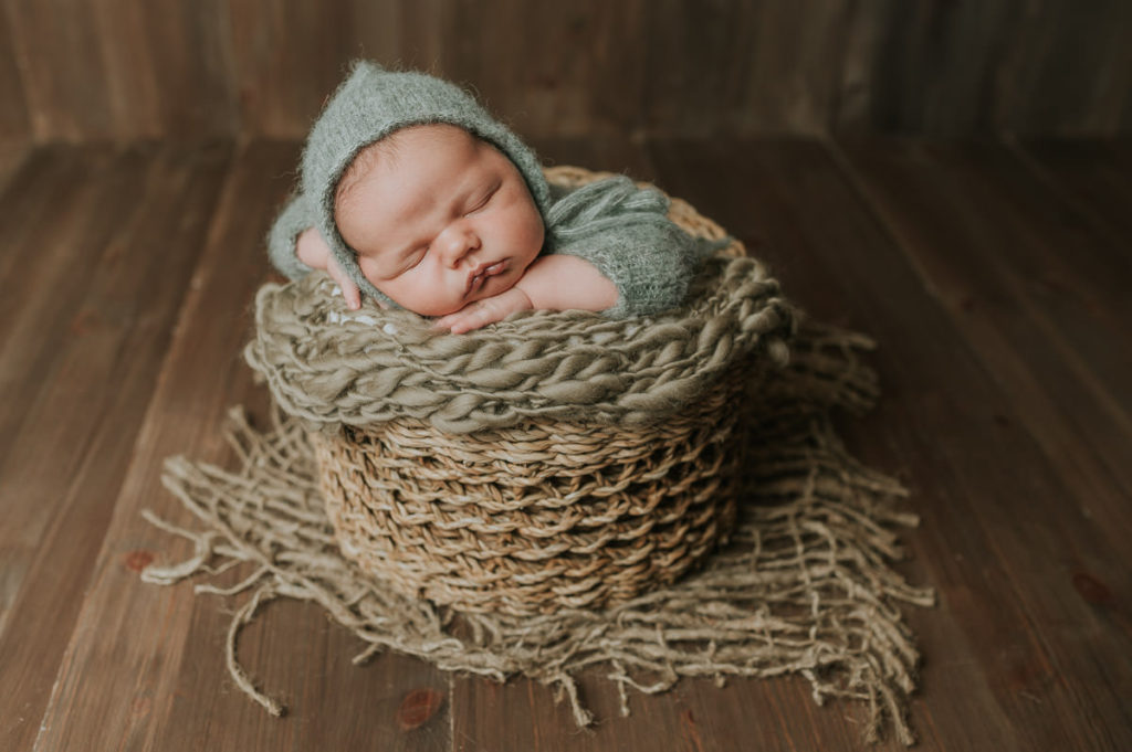 Nyfødt gutt i grønn strikket drakt  sover i en kurv på brun bakgrunn
