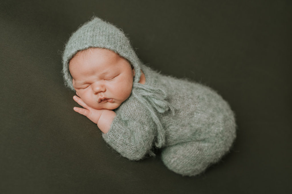 Nyfødt gutt i grønn strikket drakt  sover på grønn bakgrunn 