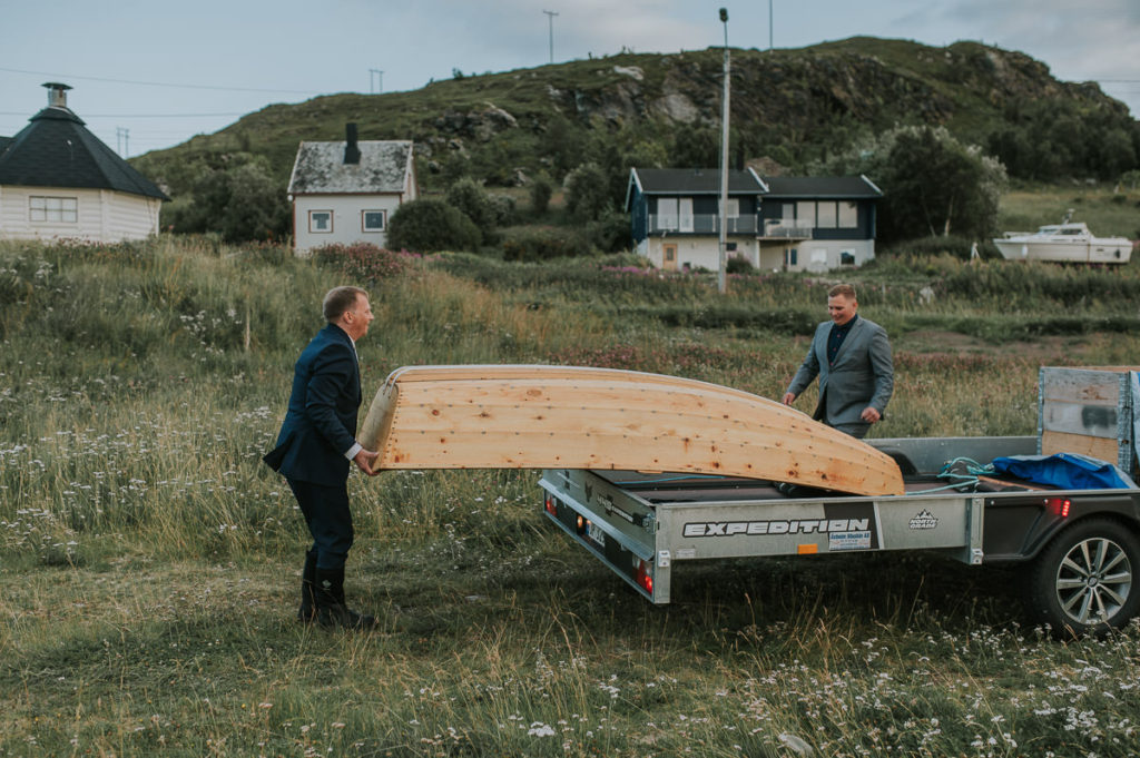 Groom and his groomsman prepare a small rowing boat for some bridal portraits on the sea  in Storekorsnes Norway