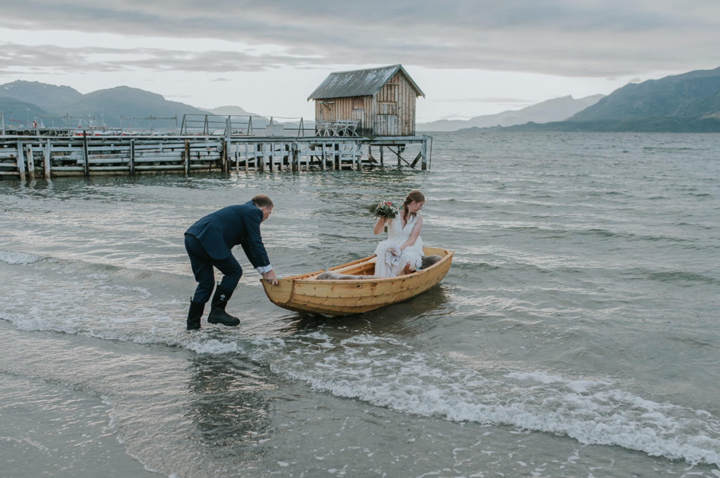 Groom pushing a rowing boat with his bride in the sea to take some bridal portraits in sunset in  Storekorsnes Alta Norway