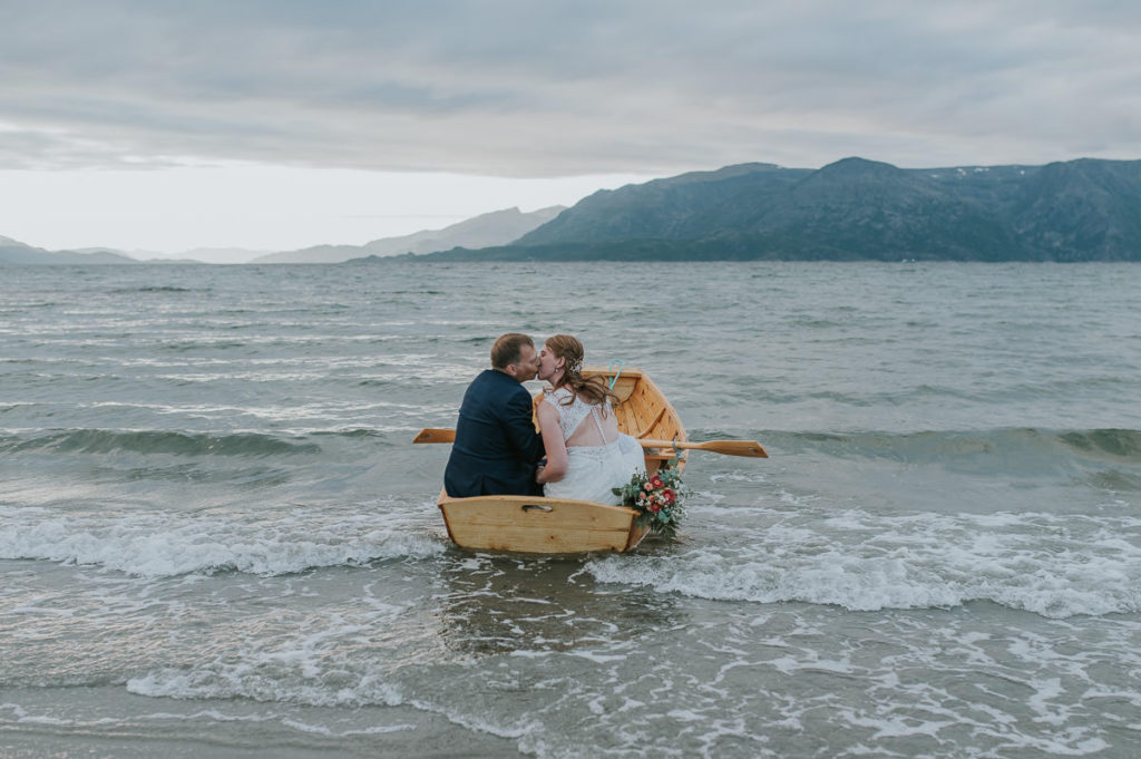 Bride and groom drinking champagne and kissing in a rowing boat with a sunset and mountain view in Storekorsnes Alta Norway