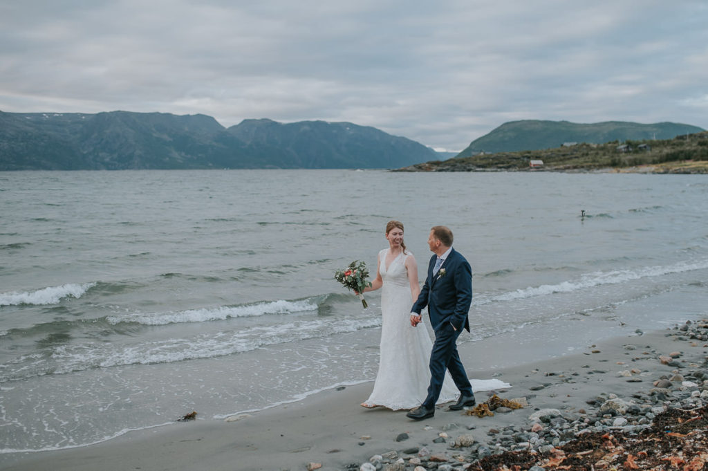Bride and groom walking on a beach with a mountain view in Storekorsnes Norway
