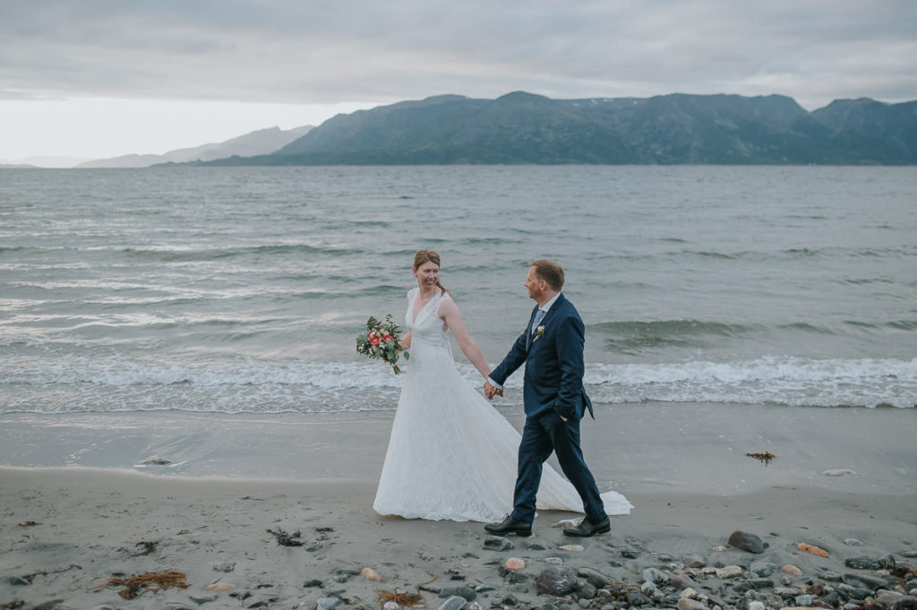 Bride and groom walking on a beach with a mountain view in Storekorsnes Norway