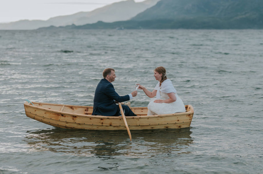 Bride and groom drinking champagne in a rowing boat with a sunset and mountain view in Storekorsnes Alta Norway