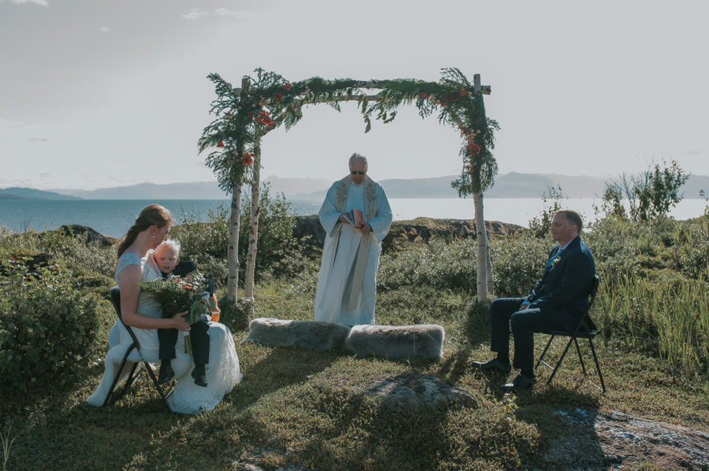 Intimate outdoor wedding ceremony under a floral arch  in Storekorsnes near Alta Norway by the fjords with a sea view and mountains