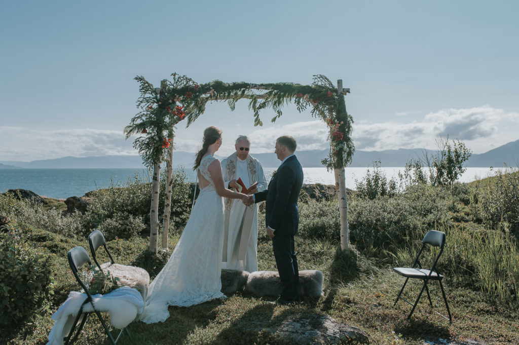 Intimate outdoor wedding ceremony under a floral arch  in Storekorsnes near Alta Norway by the fjords with a sea and mountain view