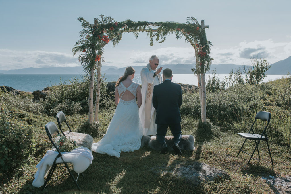 Intimate outdoor wedding ceremony under a floral arch  in Storekorsnes near Alta Norway by the fjords with a sea and mountain view
