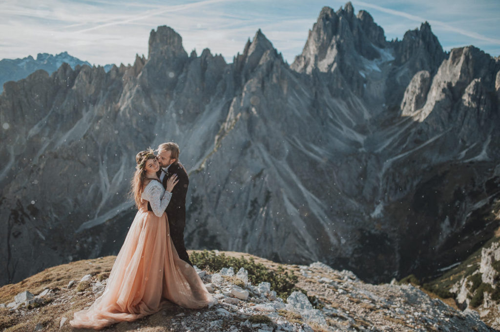 Wedding anniversary in Italian Dolomites in Northern Italy - the groom is kissing her on her chick and she is laughing 