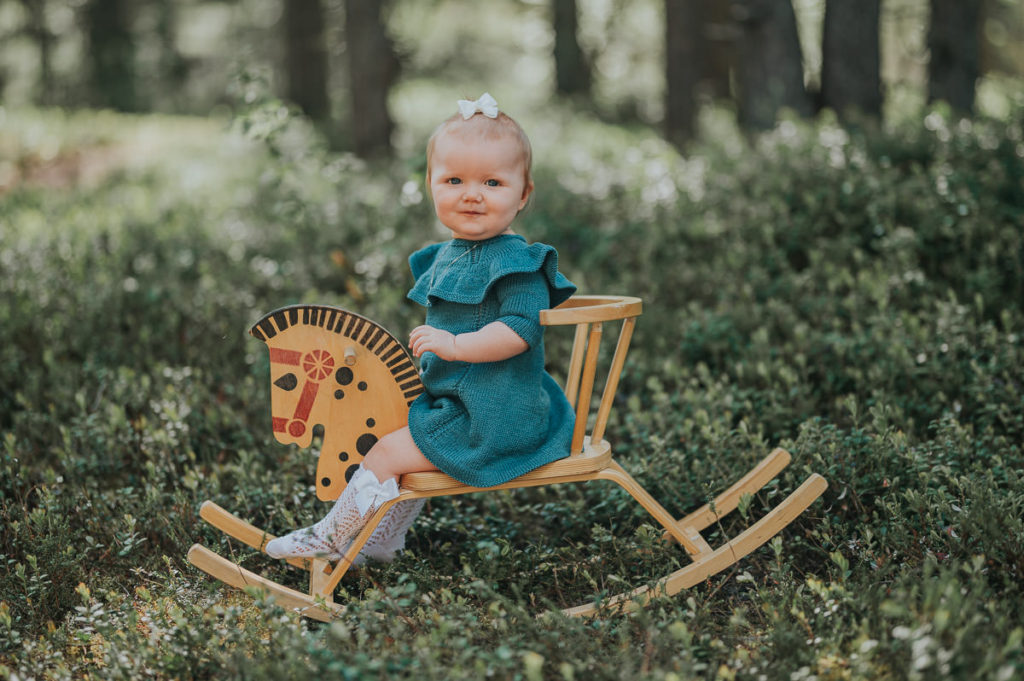 Nydelig jente på ett år sitter og gynger på en gammeldags gyngehest i en skog i Alta
