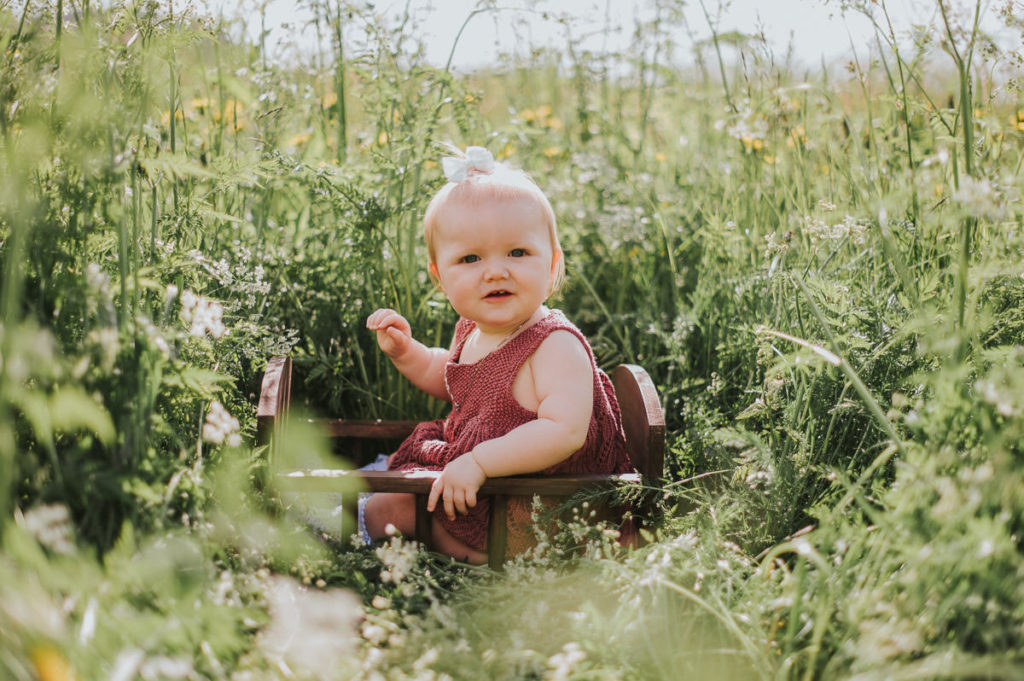 Søt baby jente i en blomstereng på sin ettårsdag