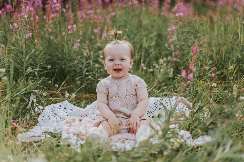 Fin jente på ett år sitter ute i en blomstereng i Alta på ettårsfoto