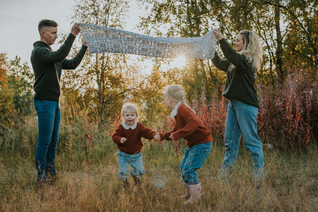 Familiefoto blant nydelige høstfarger og solnedgang i Alta - foreldre leker med sine to små døtre