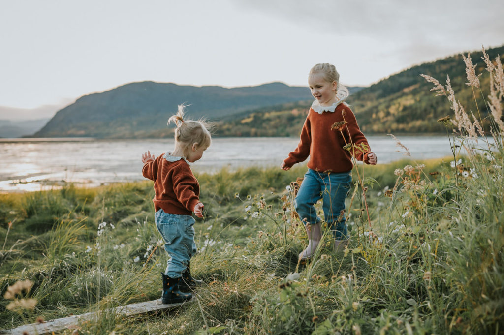 To søstre leker i fjæra i Alta med sjø og fjell i bakgrunn - familiefotografering i Alta hos TS Foto Design