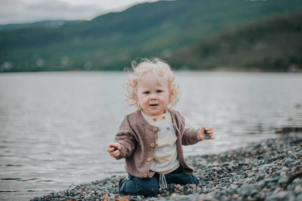 Bilde av en alvorlig ettåring i en fjæra i Alta med små stein i hendene