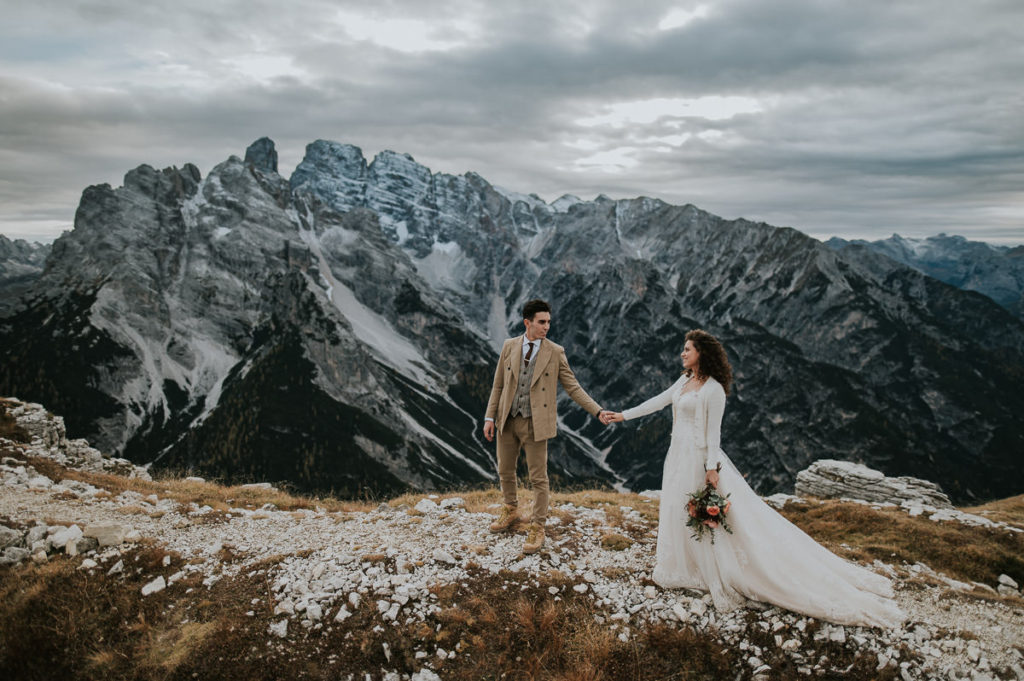 Bride and groom holding hands and hiking in the Italian Dolomites mountains  on the day of their adventure elopement 