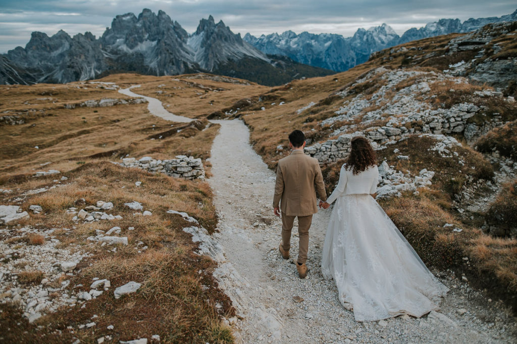 Bride and groom walking on a muntain trail in Italian Dolomites on the day of their elopement