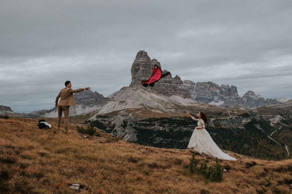 Groom throwing a jacket to his bride in front of a beautiful Italian alps