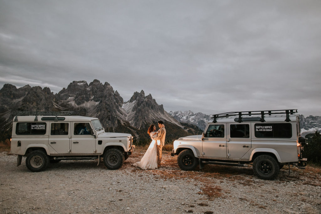 Bridal portrait between two jeeps in high mountains Italian Alps 