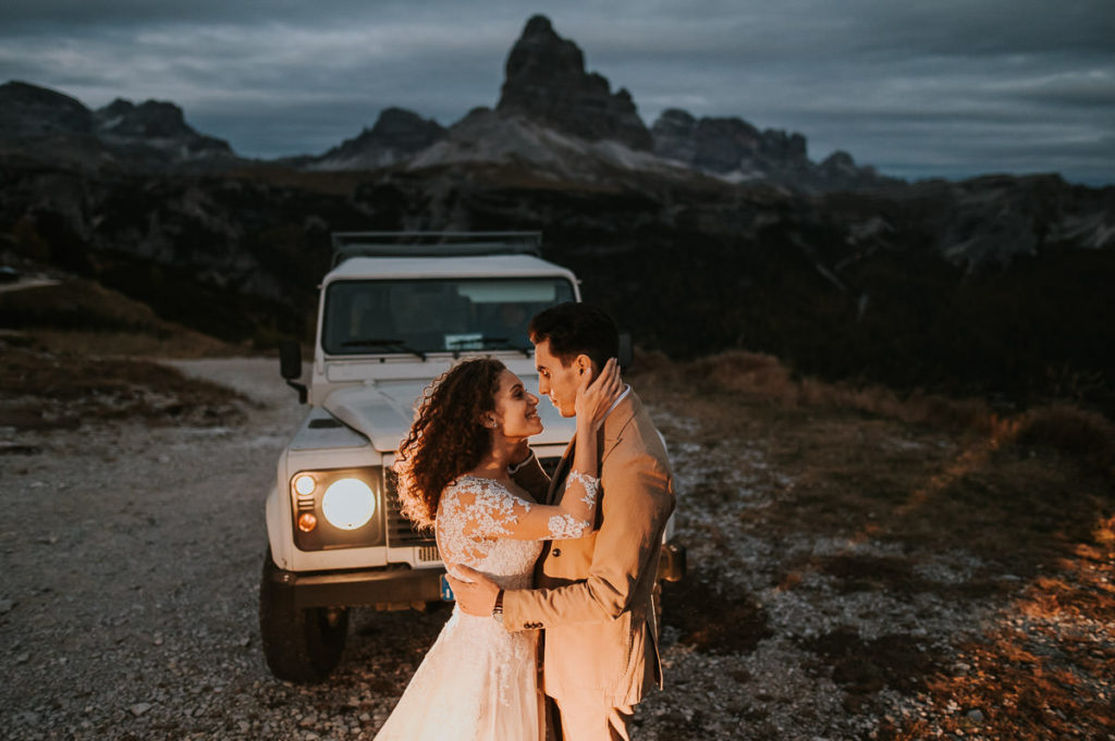 Bride and groom portrait in darkness in front of a jeep in the Italian Alps