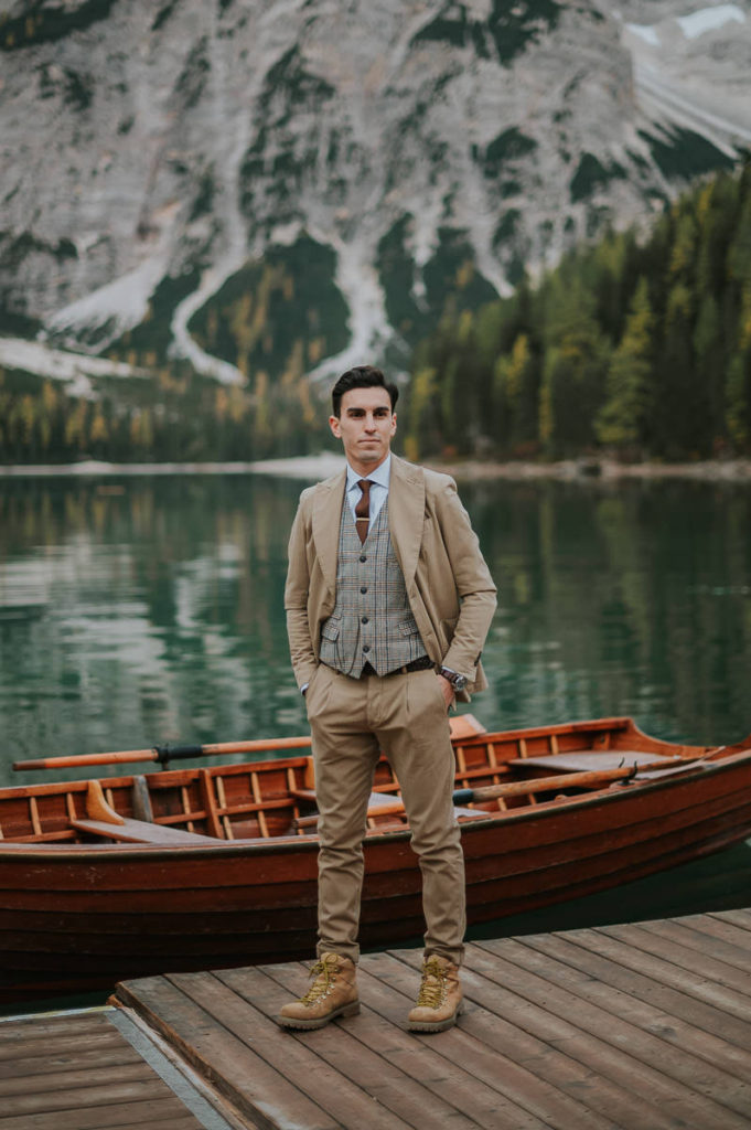 Handsome groom in a beige suite in front Lago di Braies in Italy on the day of his elopement