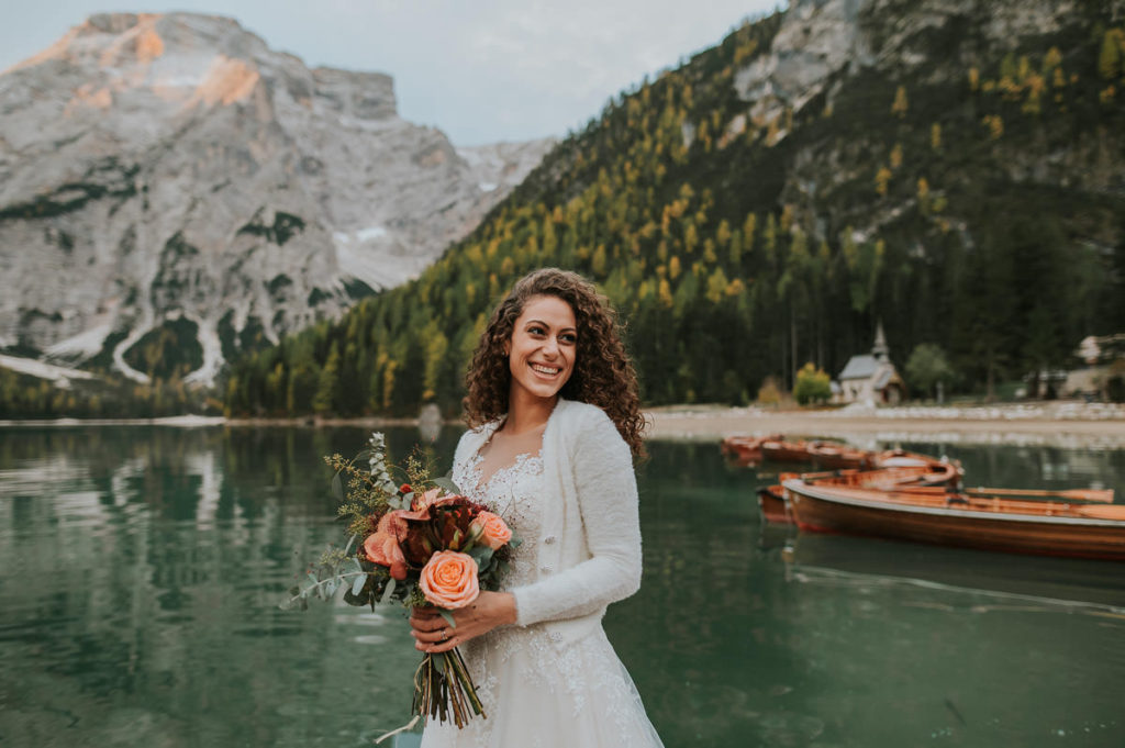 Gorgeous italian bride with curly hair in front of a beautiful green mountain lake in Italian Dolomites