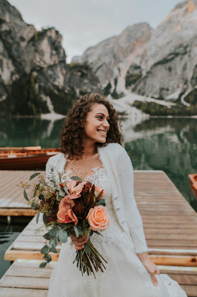 Gorgeous italian bride with curly hair in front of a beautiful green mountain lake in Italian Dolomites - Lago di Braies elopement
