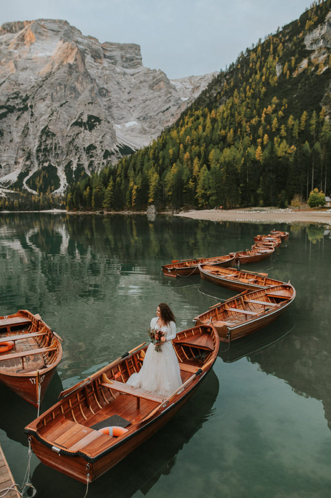 Gorgeous italian bride with curly hair in front of a beautiful green mountain lake in Italian Dolomites - Lago di Braies elopement