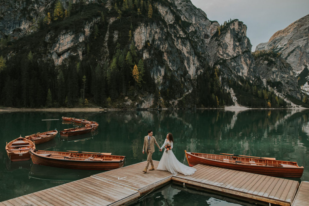 Bride and groom holding hands and walking by the Lake di Braies Pragser Wildsee in Dolomites Italy on the day of their elopement wedding