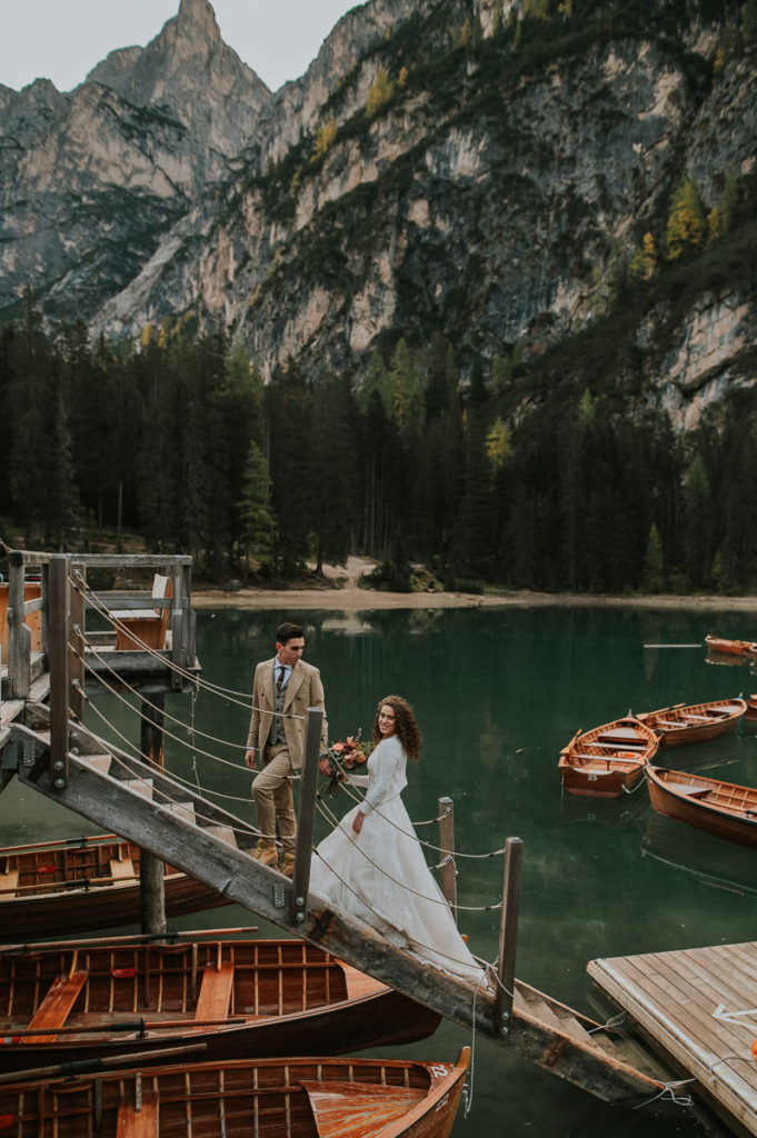 Bride and groom holding hands and walking by the Lake di Braies Pragser Wildsee in Dolomites Italy on the day of their elopement wedding